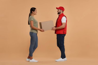 Gülümseyen kurye, açık kahverengi arkaplandaki alıcıya paket veriyor