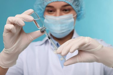 Şırıngayı cam şişeden alınan ilaçlarla dolduran doktor açık mavi arka plan, seçici odak