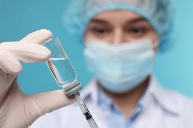 Şırıngayı cam şişeden alınan ilaçlarla dolduran doktor açık mavi arka plan, seçici odak