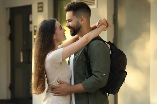 Long-distance relationship. Man with backpack hugging with his girlfriend near house entrance outdoors