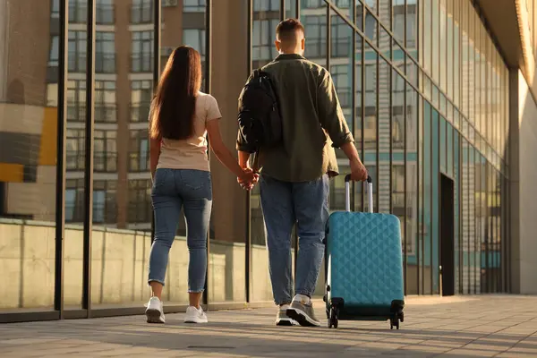 Long-distance relationship. Young couple with luggage walking near building outdoors, back view