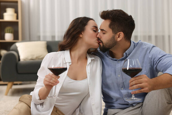 Passionate young couple with glasses of wine kissing at home