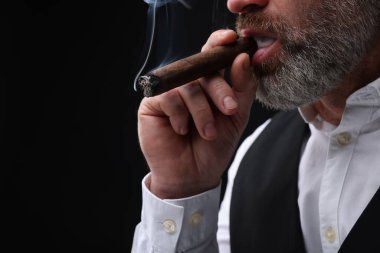 Siyah arka planda puro içen sakallı adam, yakın plan. Metin için boşluk