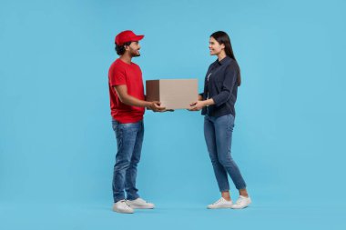 Gülümseyen kurye açık mavi arkaplandaki alıcıya paket veriyor