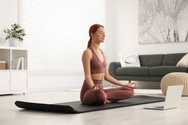 Evdeki yoga minderinde Padmasana egzersizi yapan güzel bir genç kadın. Lotus pozu