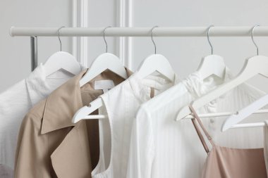 Beyaz duvarın yanında farklı şık kadın kıyafetleriyle dizilin, yakın plan.