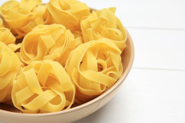 Beyaz ahşap masada, kasede çiğ tagliatelle makarnası, yakın plan.