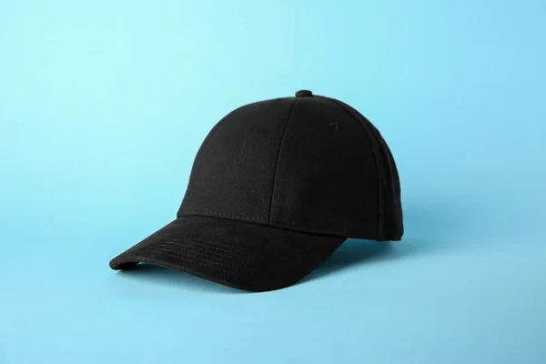 Stylish black baseball cap on light blue background