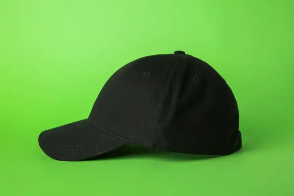 Stylish black baseball cap on light green background