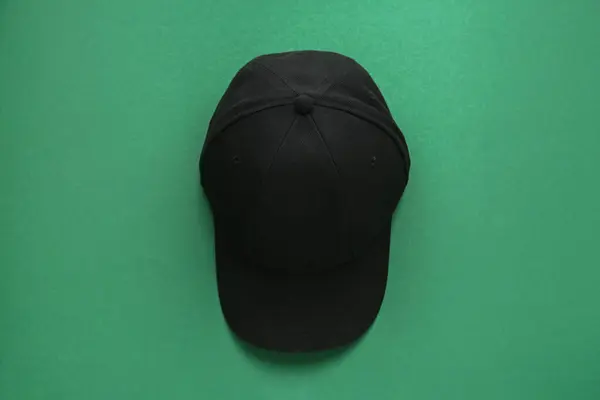 Stylish black baseball cap on green background, top view