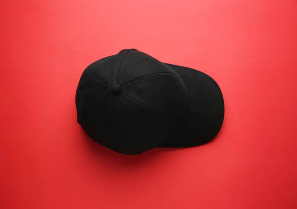 Stylish black baseball cap on red background, top view