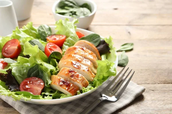 Eating delicious salad with chicken, cherry tomato and spinach served on wooden table, closeup. Space for text