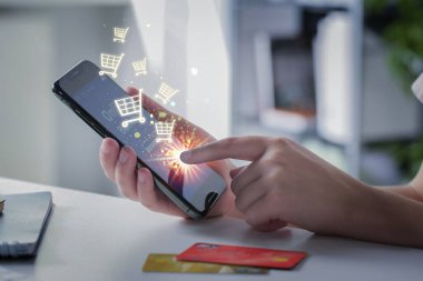 İnternetten satın almak için akıllı telefon kullanan bir kadın, yakın plan. Cihaz ekranından alışveriş arabası simgeleri uçuyor