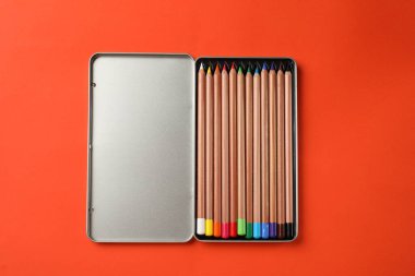 Turuncu arka planda renkli pastel kalemlerle dolu bir kutu, üst manzara. Malzemeler çiziliyor