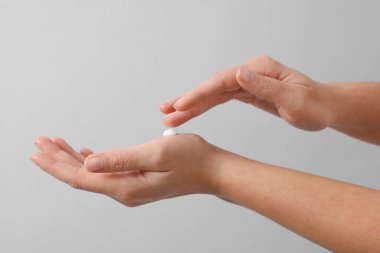 Woman applying cosmetic cream onto hand on light grey background, closeup