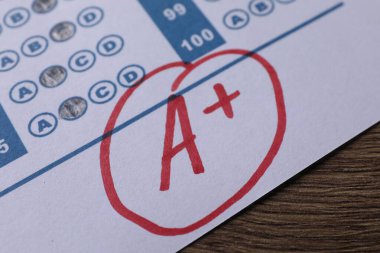 Okul derecesi. Kırmızı harfli cevap kağıdı A ve artı sembolü ahşap masada, yakın plan.