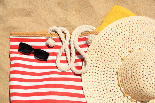 Striped beach bag, sunglasses, towel and hat on sand, flat lay