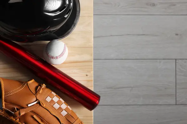 Baseball bat, batting helmet, leather glove and ball on wooden bench indoors, top view. Space for text