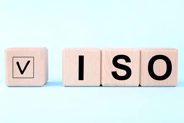 International Organization for Standardization. Wooden cubes with check mark and abbreviation ISO on light blue background