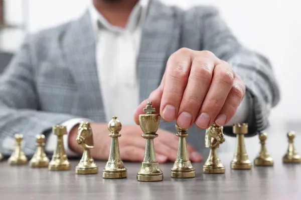 Man with chess pieces at wooden table indoors, closeup