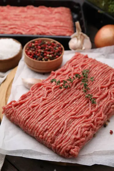 Fresh raw ground meat, thyme and peppercorns on table, closeup