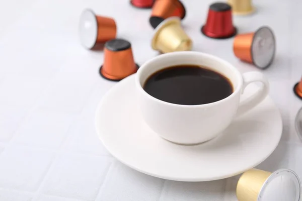Cup of coffee and capsules on white tiled table, closeup. Space for text
