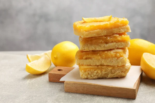 Stacked tasty lemon bars on light grey table, closeup. Space for text