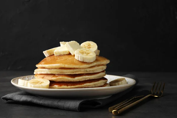 Delicious pancakes with bananas, butter and honey on dark table. Space for text