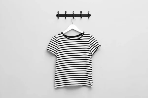 Hanger with striped T-shirt on light grey wall
