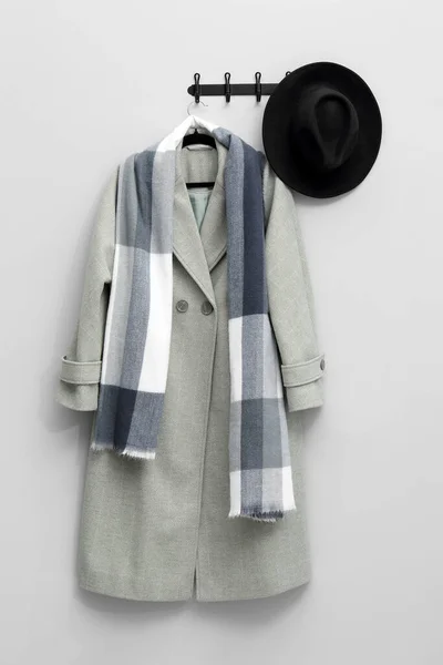 Hanger with coat, scarf and hat on light grey wall