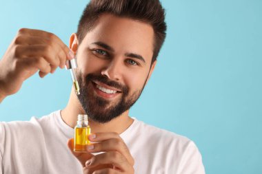 Açık mavi arkaplanda kozmetik serumu olan yakışıklı bir adam.