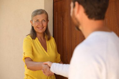Friendly relationship with neighbours. Happy senior woman and man shaking hands near house outdoors