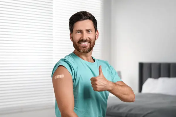 Man with sticking plaster on arm after vaccination showing thumbs up in bedroom