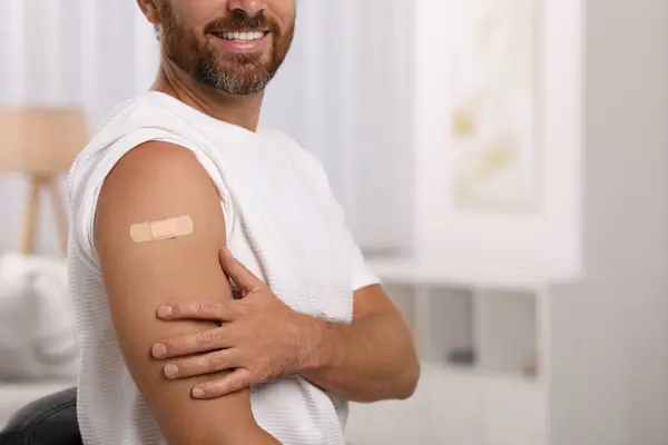 Man with sticking plaster on arm after vaccination at home, closeup. Space for text