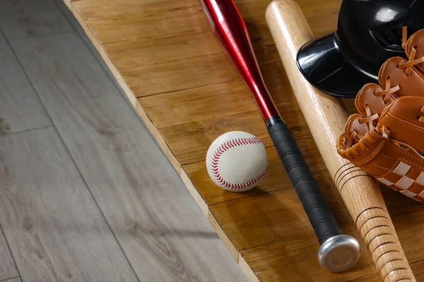 Baseball bats, batting helmet, leather glove and ball on wooden bench indoors, closeup. Space for text