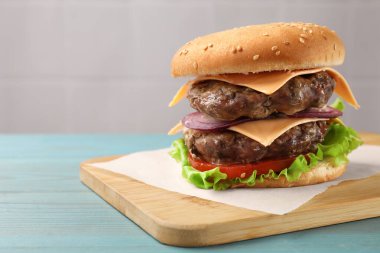 Açık mavi ahşap masada köfteli, peynirli ve sebzeli leziz hamburger.