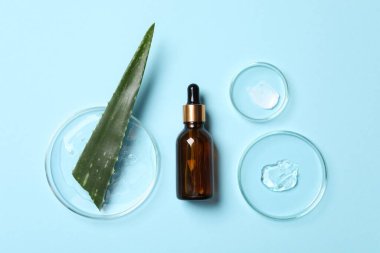 Bir şişe kozmetik serumu, aloe vera yaprağı ve üzerinde açık mavi arkaplan örnekleri olan petri kapları.