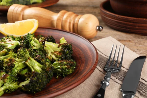 Tasty fried broccoli with lemon served on wooden table, closeup