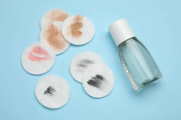 Bottle of makeup remover and dirty cotton pads on light blue background, flat lay