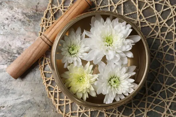Tibetan singing bowl with water, beautiful chrysanthemum flowers and mallet on table, top view