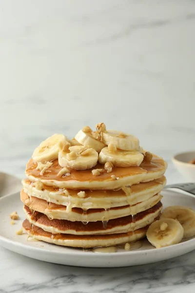 Delicious pancakes with bananas, walnuts and honey on white marble table. Space for text