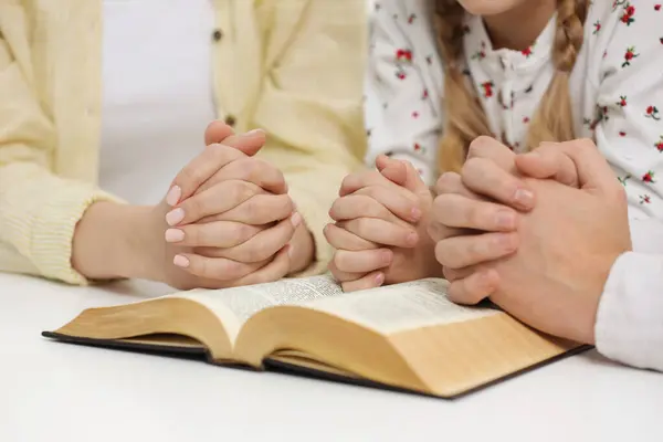 Girl and her godparents praying over Bible together at table indoors, closeup
