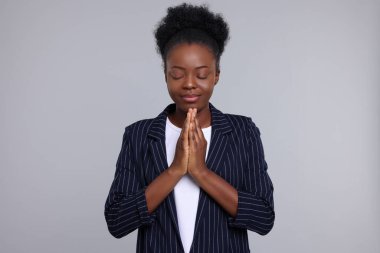 Elleri bağlı bir kadın açık gri arka planda Tanrı 'ya dua ediyor.