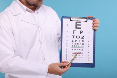 Oftalmolog açık mavi arkaplan ve yakın plan görme testine işaret ediyor.