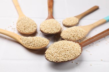 Beyaz döşeme üzerinde kuru kinoa tohumları olan kaşıklar, yakın plan.