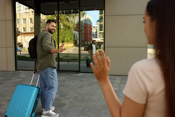 Long-distance relationship. Woman waving to her boyfriend with luggage outdoors, selective focus