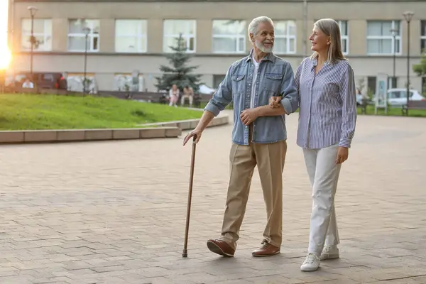 Senior man with walking cane and mature woman outdoors. Space for text