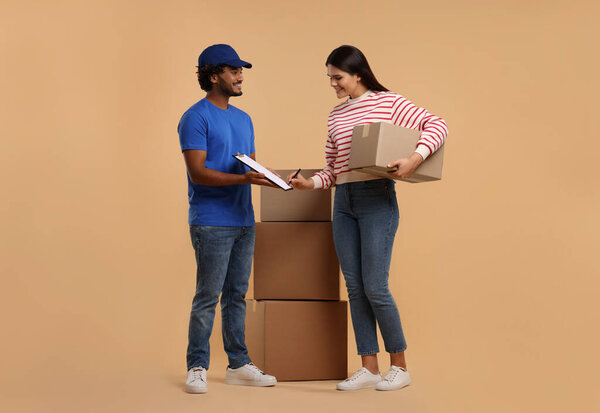 Smiling woman signing order receipt on light brown background. Courier delivery