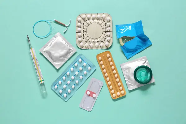 stock image Contraceptive pills, condoms, intrauterine device and thermometer on turquoise background, flat lay. Different birth control methods