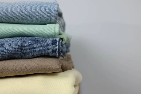 Stack of different folded clothes near grey wall, closeup. Space for text
